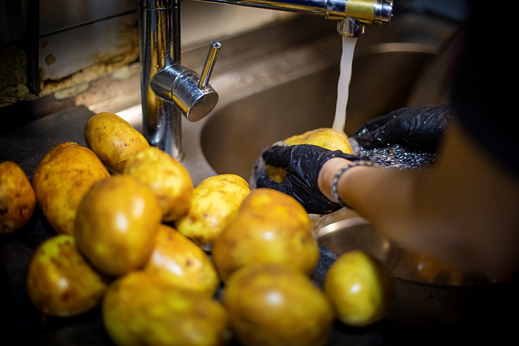 Hands wearing black gloves washing fresh potatoes under running water at a kitchen sink – Yummy Cooking Treats