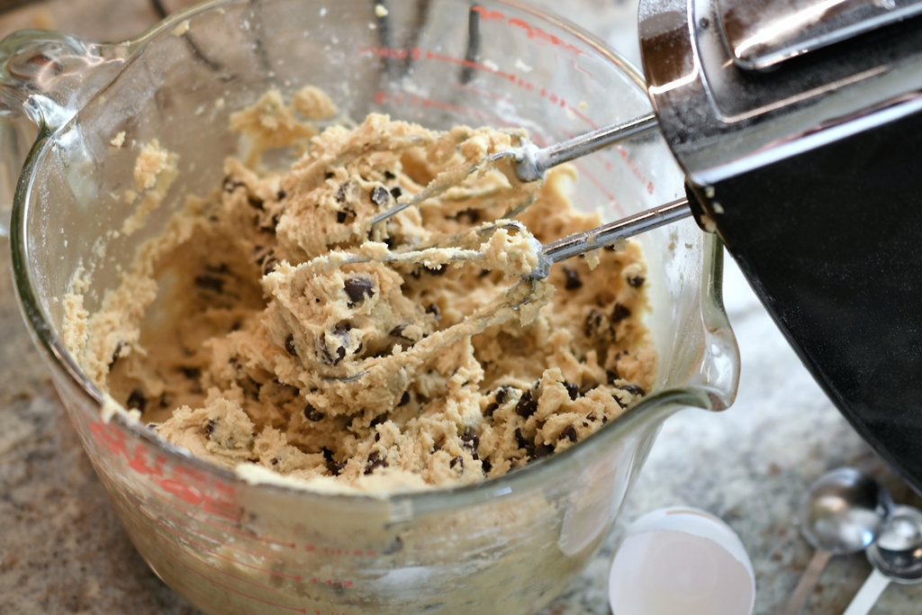 Thick, creamy chocolate chip cookie dough in a mixing bowl with an electric hand mixer – Yummy Cooking Treats