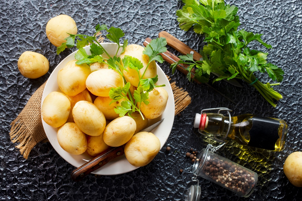 Bowl of raw peeled potatoes with fresh parsley, olive oil, and peppercorns on dark textured background – Yummy Cooking Treats