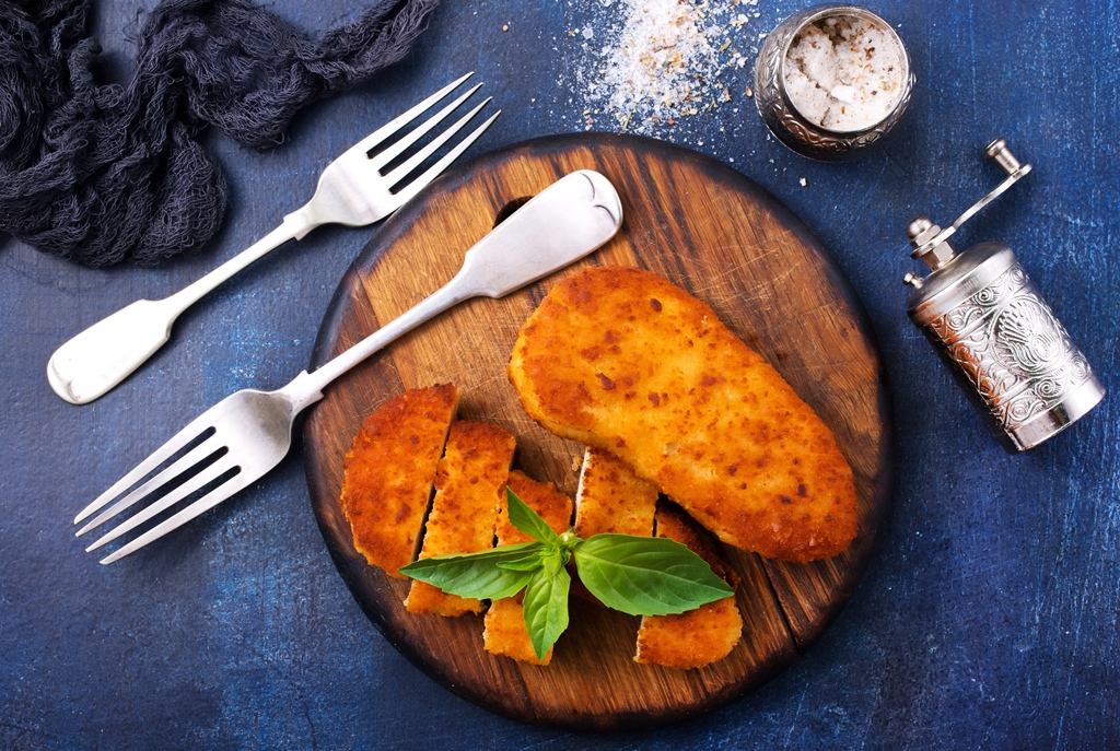 Golden-brown fried chicken breast on wooden board with basil garnish – Yummy Cooking Treats' chicken parmesan step