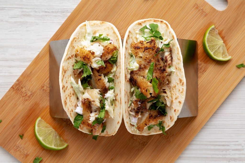 Top view of grilled fish tacos in flour tortillas with shredded cabbage, cilantro, and lime crema on a wooden board – Yummy Cooking Treats