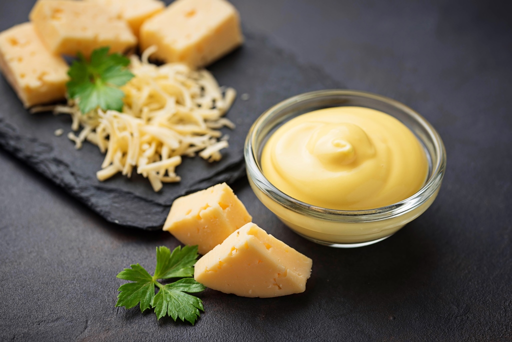 Creamy homemade Swiss cheese sauce in a glass bowl with shredded and cubed cheese on a slate board