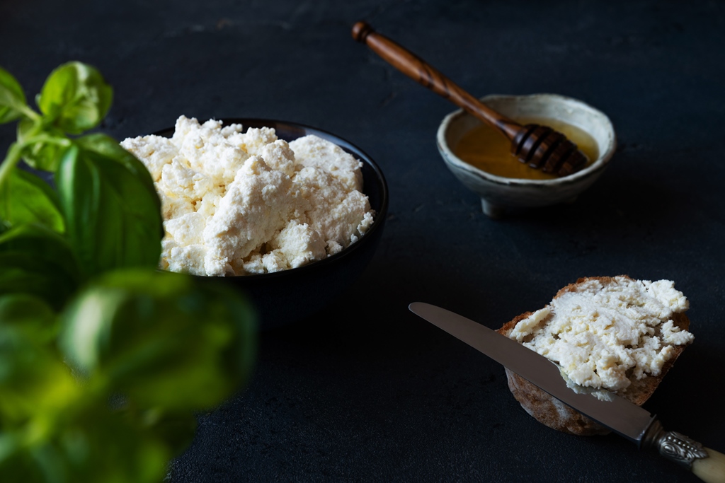 Homemade ricotta cheese in a bowl with basil and honey on the side – a creamy lasagna filling from Yummy Cooking Treats