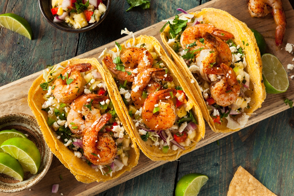 Three shrimp tacos topped with mango salsa, red onion, cheese, and cilantro in corn tortillas on a wooden board – Yummy Cooking Treats