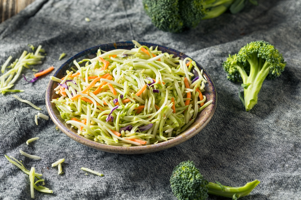Colorful bowl of fresh broccoli slaw with carrots and cabbage – Yummy Cooking Treats veggie mix on rustic cloth with broccoli florets