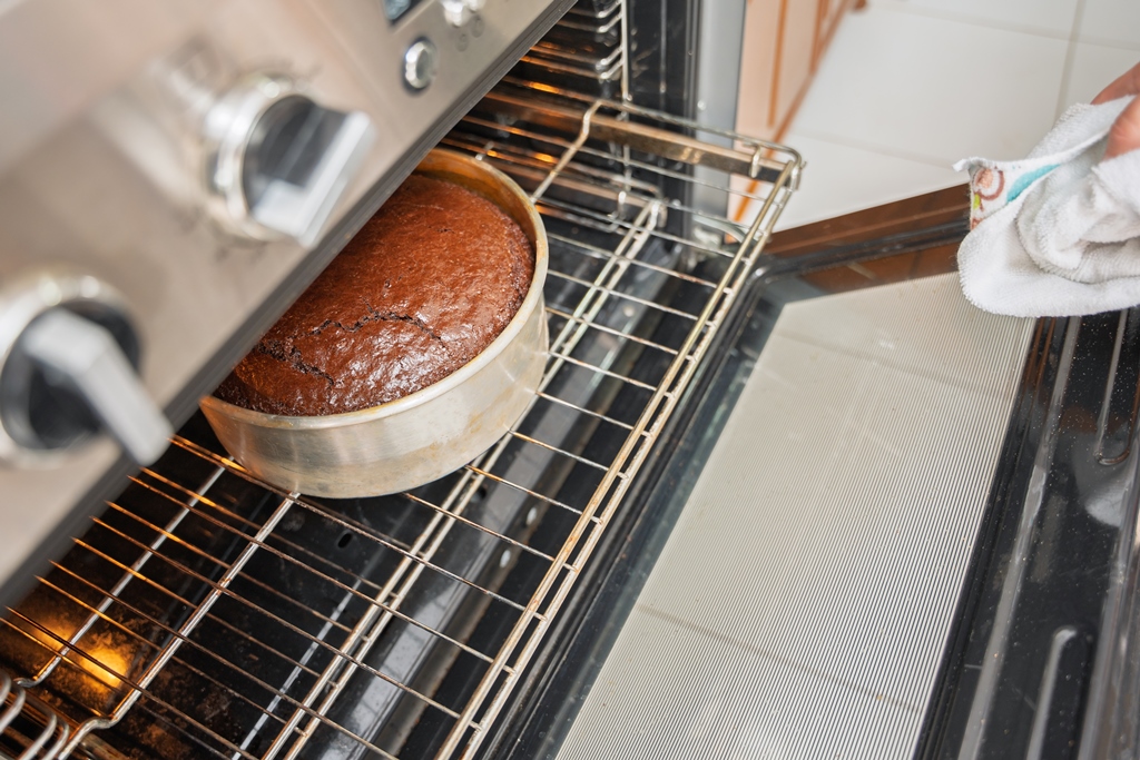 A rich chocolate cake baking in a round metal pan inside an oven, just about ready – Yummy Cooking Treats dessert recipe
