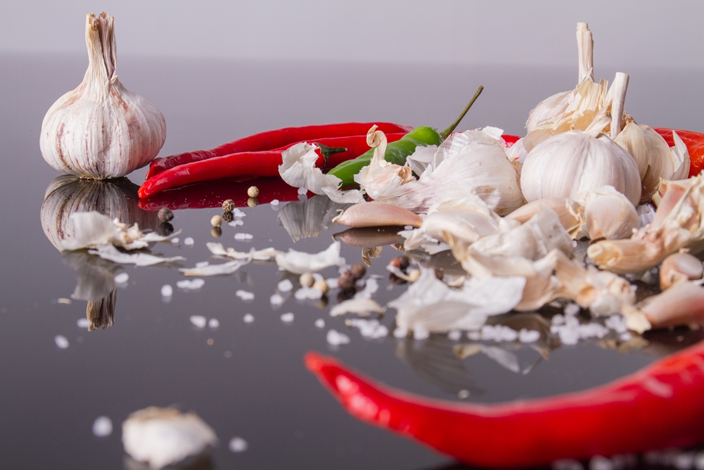Close-up of garlic bulbs, chili peppers, and scattered spices on a reflective black surface – Yummy Cooking Treats
