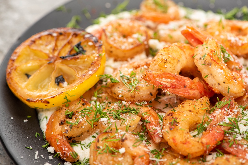 Close-up of garlic butter shrimp topped with dill and Parmesan, served with grilled lemon slices on a black plate – Yummy Cooking Treats