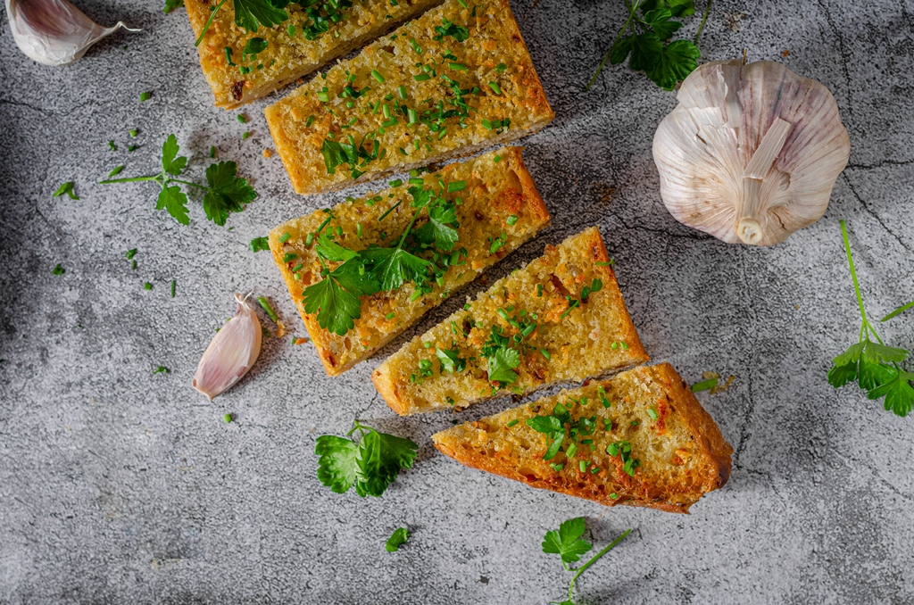 Slices of homemade garlic butter bread topped with fresh parsley and chives on a stone surface – Yummy Cooking Treats