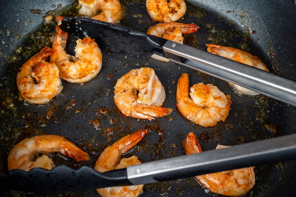 Juicy garlic butter shrimp sizzling in a hot pan with tongs turning them – Yummy Cooking Treats