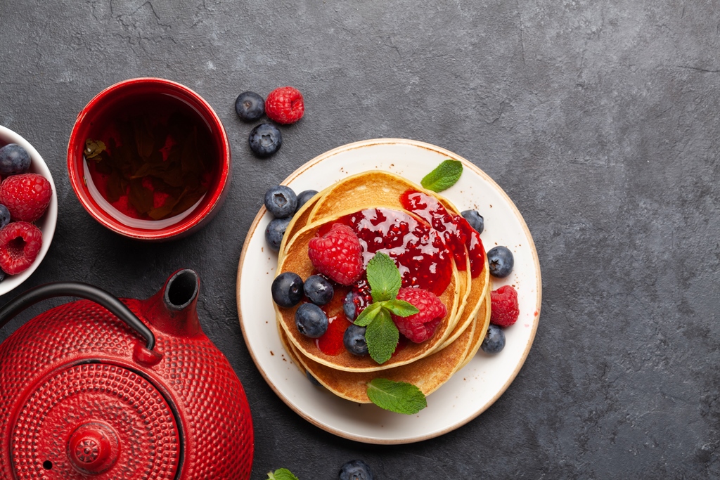A plate of almond flour pancakes topped with raspberry sauce, fresh blueberries, raspberries, and mint, served with tea – Yummy Cooking Treats