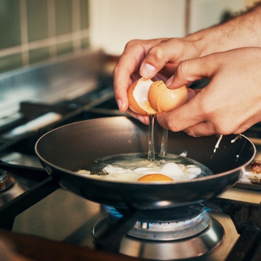 Close-up of hands cracking eggs into a hot frying pan on a gas stove—step one for fried rice or breakfast prep by Yummy Cooking Treats